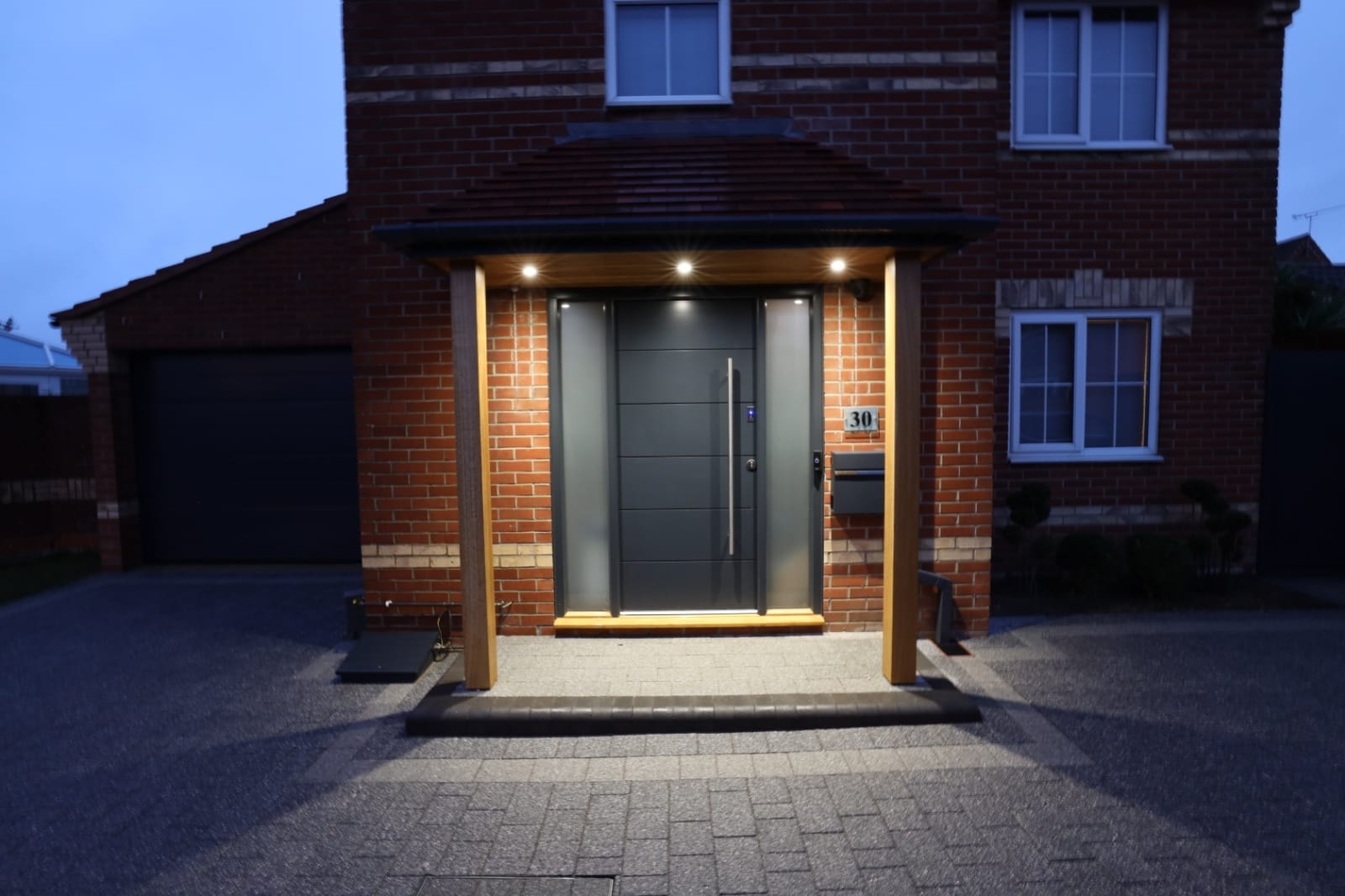 Modern entrance door with oak canopy downlights at dusk